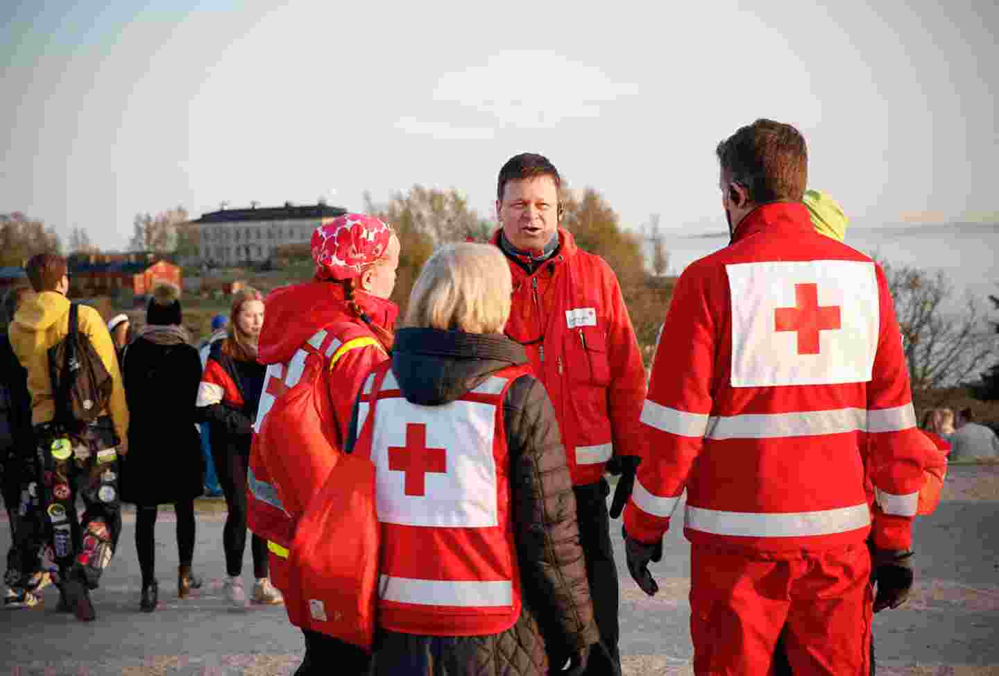 Neljä ensiapupäivystäjää Punaisen Ristin varusteissa keskustelee ulkoilmassa väkijoukon keskellä.