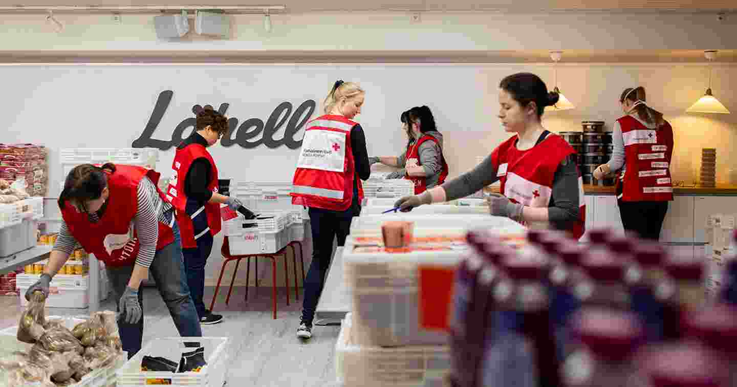 Kuusi henkilöä Punaisen Ristin vapaaehtoisliiveissä järjestelee ruoka-pakkauksia.