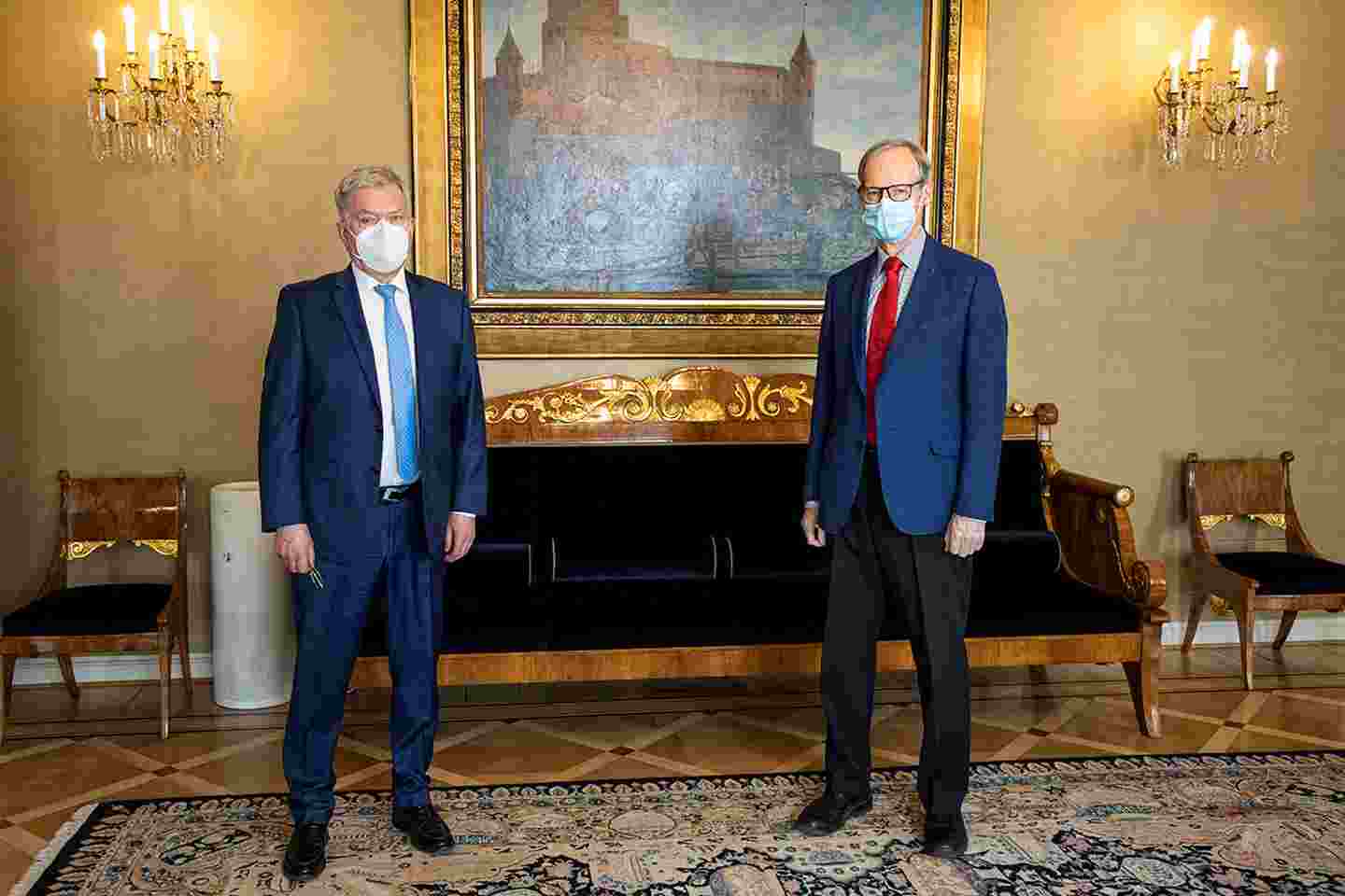 Sauli Niinistö ja Pertti Torstila kasvoillaan maskit seisovat taululla ja kristallikruunuilla sisustetussa huoneessa.