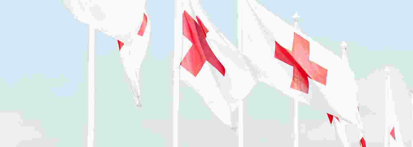 Punaisen Ristin liput liehuvat tuulessa vaaleansinistä taivasta vasten.