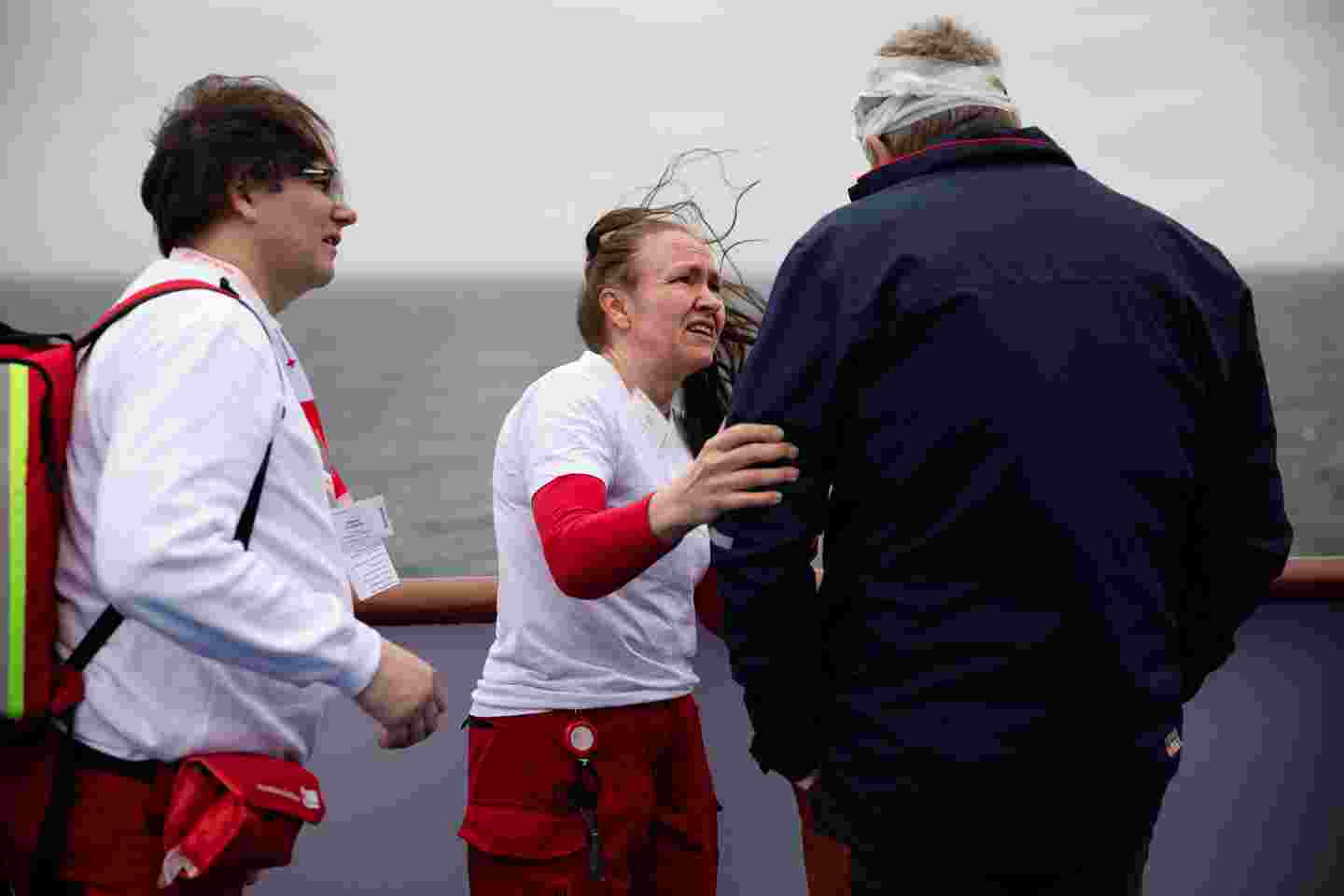 Kaksi Ruotsin Punaisen Ristin vapaaehtoista keskustelevat maalihenkilön kanssa, jolla on sideharsoa pään ympärillä. Taustalla näkyy itämeri. Kuva on otettu laivan kannelta.