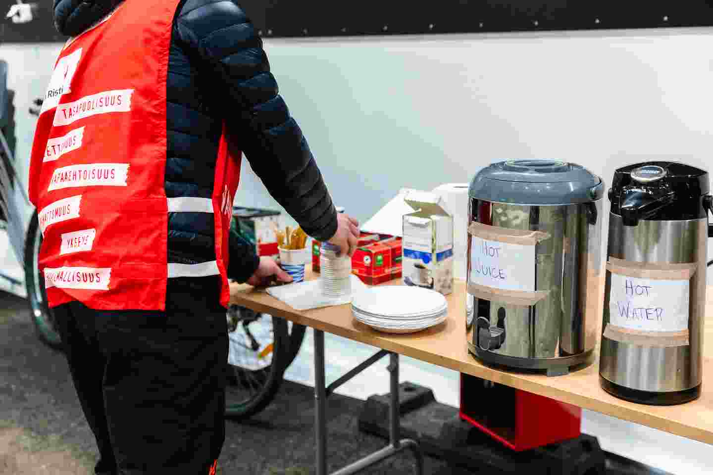 Punaisen Ristin vapaaehtoinen järjestelee pöytää, jolla on kuumia juomia termosastioissa.