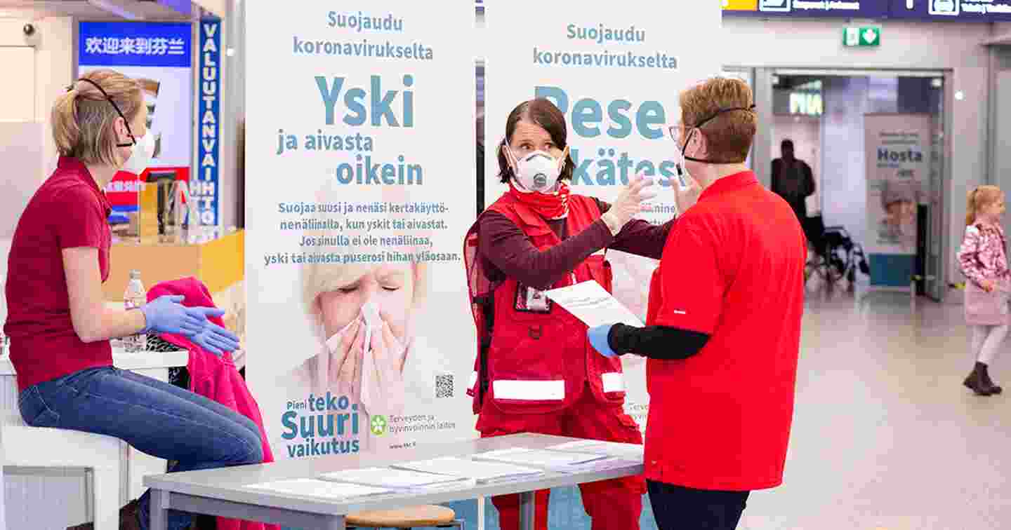 Kolme Punaisen Ristin liiveihin varustautunutta henkilöä koronaneuvontapisteellä Helsinki-Vantaan lentoasemalla.