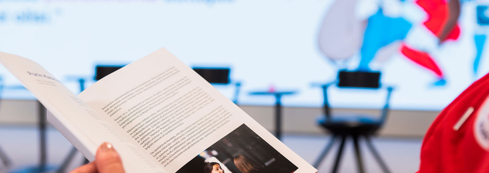 Henkilö selailee kädessään olevaa esitettä. 